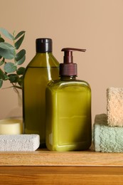 Photo of Solid shampoo bar and bottles of cosmetic product on wooden table near beige wall, closeup