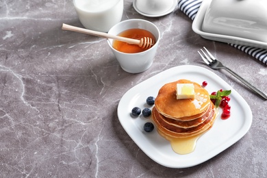 Stack of tasty pancakes with berries, butter and honey on table