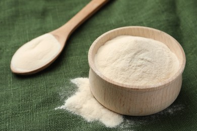 Wooden bowl and spoon of agar-agar powder on green tablecloth, closeup