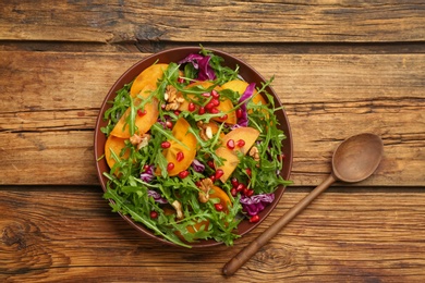 Photo of Delicious persimmon salad served on wooden table, flat lay