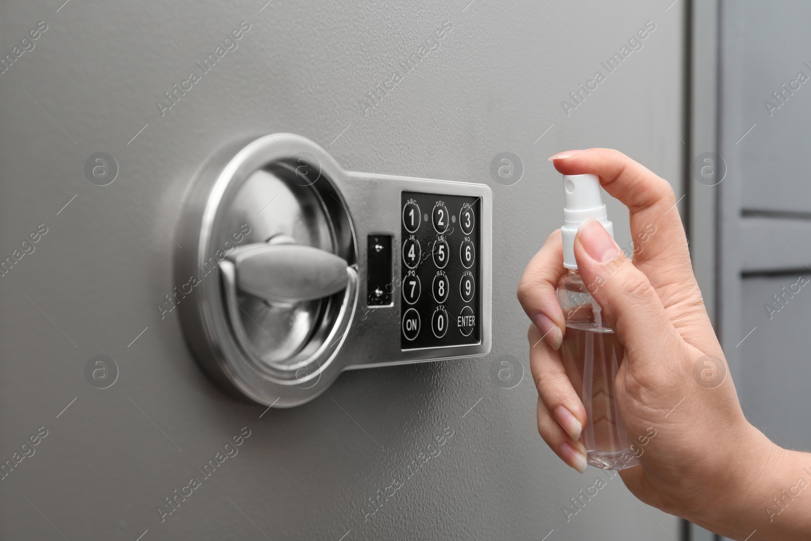 Photo of Woman spraying antiseptic onto keypad of modern safe, closeup