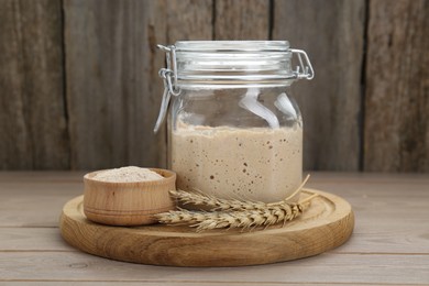 Photo of Leaven and ears of wheat on beige wooden table