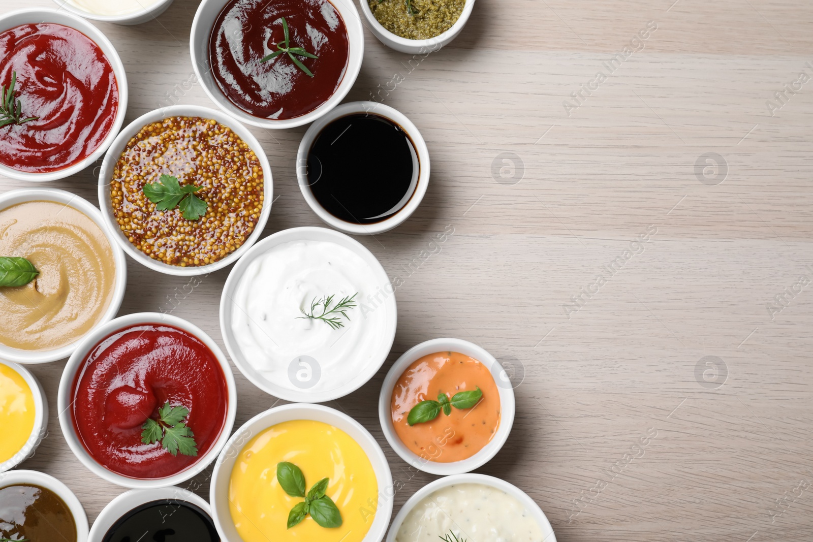 Photo of Many different sauces and herbs on wooden table, flat lay. Space for text