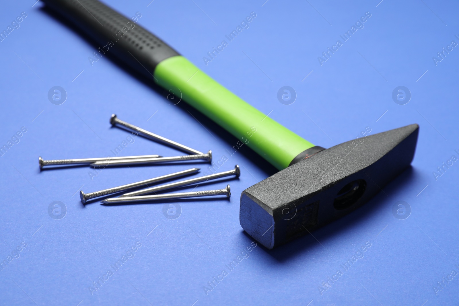 Photo of Hammer and metal nails on blue background, closeup