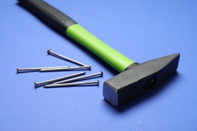 Photo of Hammer and metal nails on blue background, closeup