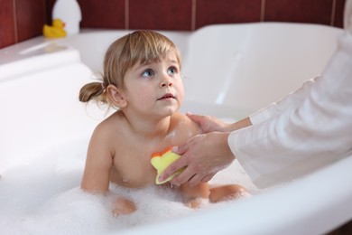 Mother washing her little daughter with sponge in bathtub, closeup