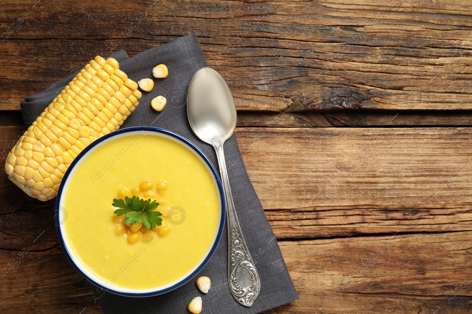 Photo of Delicious creamy corn soup served on wooden table, top view. Space for text