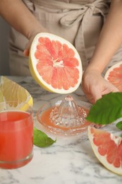 Woman squeezing pink pomelo juice at white marble table, closeup