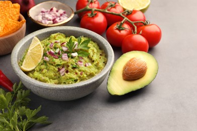 Photo of Bowl of delicious guacamole, nachos chips and ingredients on grey table, closeup. Space for text