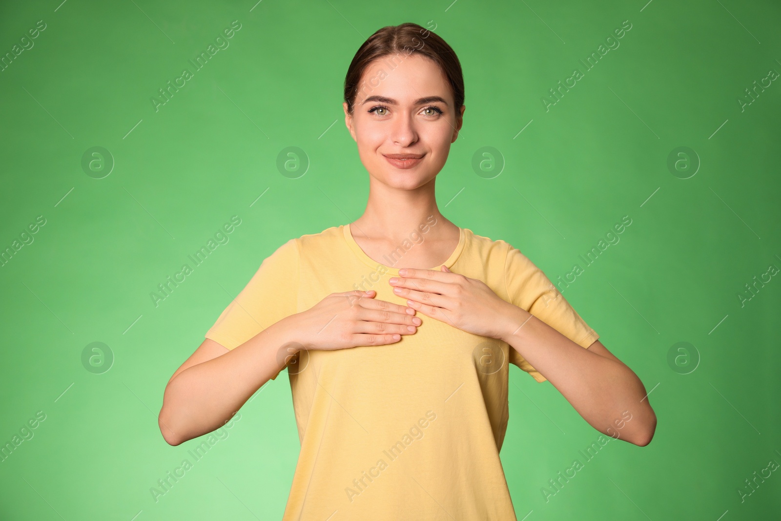 Photo of Young woman holding hands near chest on green background, closeup