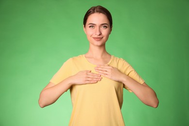 Photo of Young woman holding hands near chest on green background, closeup