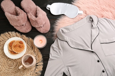 Photo of Flat lay composition with fluffy slippers and pajamas on black wooden background. Comfortable home outfit