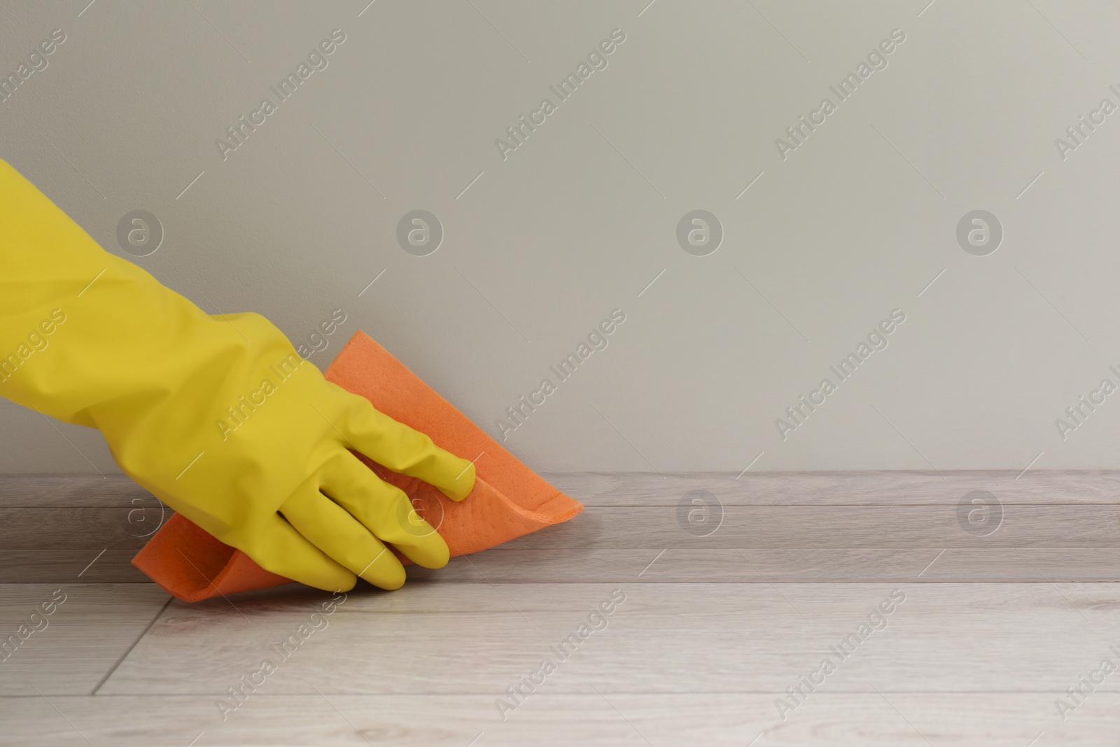 Photo of Woman in protective glove cleaning plinth with sponge cloth indoors, closeup. Space for text