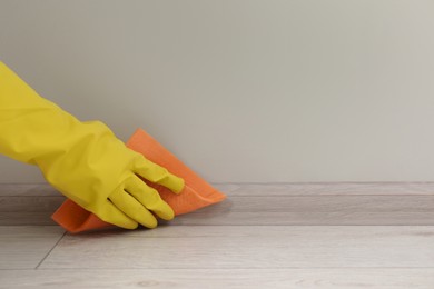 Woman in protective glove cleaning plinth with sponge cloth indoors, closeup. Space for text