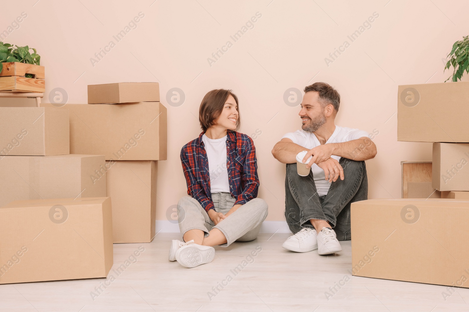 Photo of Happy couple with takeaway coffee resting on floor in new apartment. Moving day