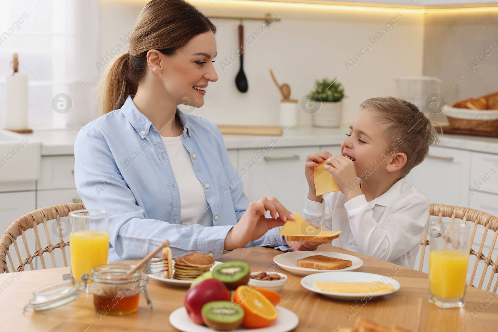 Photo of Mother and her cute little son having breakfast at table in kitchen