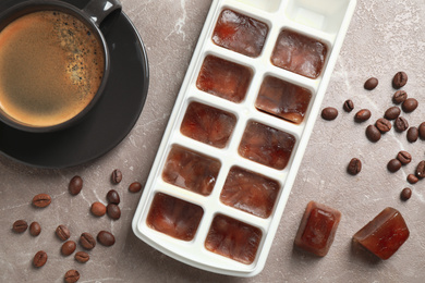 Ice cubes, cup of coffee and beans on grey table, flat lay