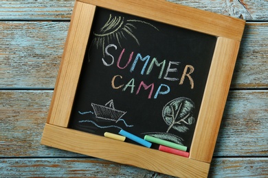 Blackboard with text SUMMER CAMP, drawings and chalk sticks on wooden background, top view