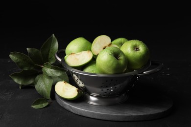 Ripe green apples with water drops and leaves on black table