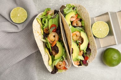 Delicious tacos with shrimps, avocado and lime on light grey table, flat lay