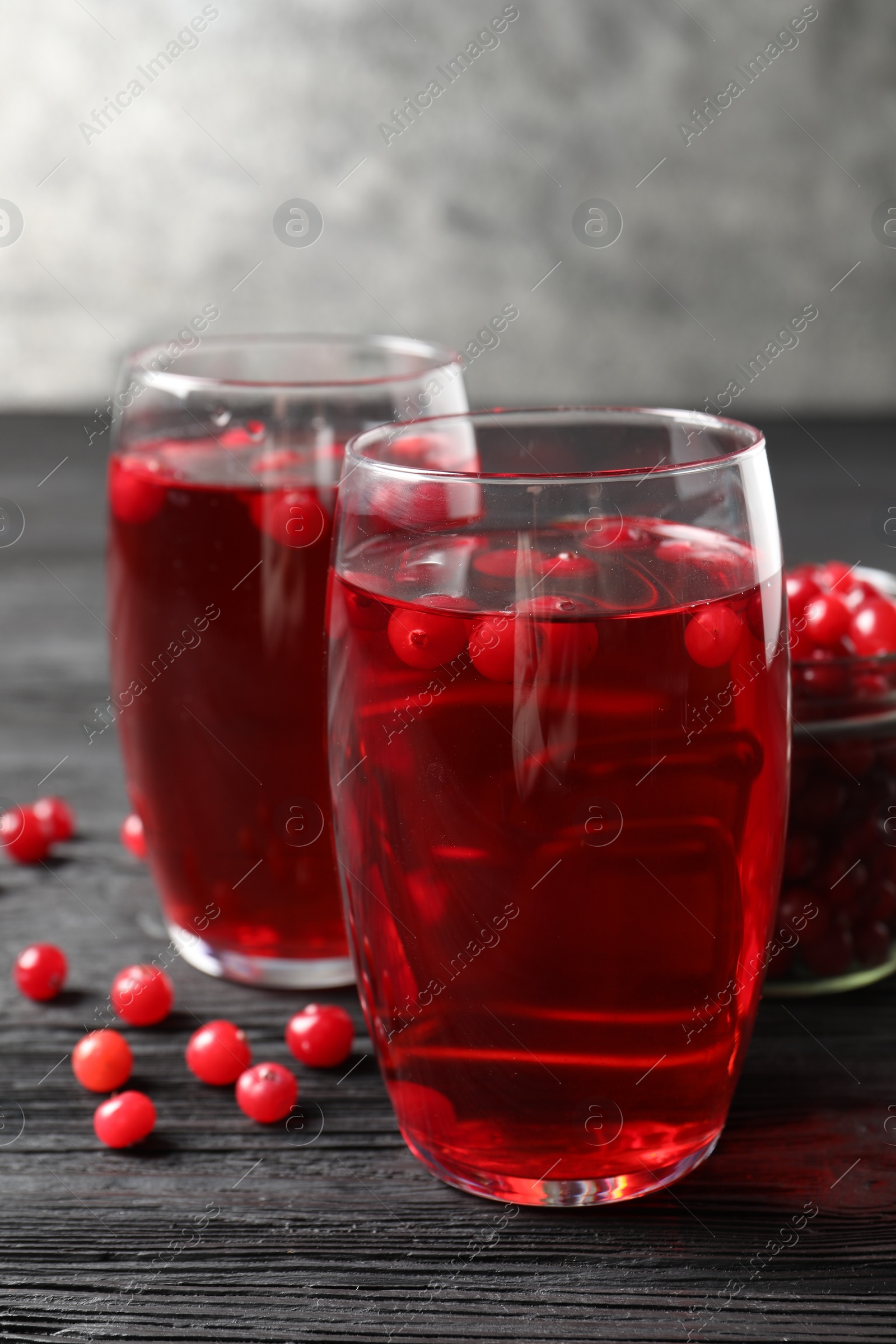 Photo of Tasty cranberry juice in glasses and fresh berries on black wooden table, closeup