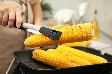 Photo of Woman cooking fresh corn cobs on grill pan, closeup