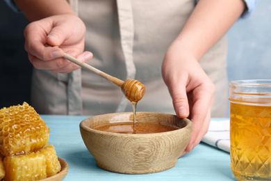 Photo of Woman with honey and dipper at blue wooden table, closeup