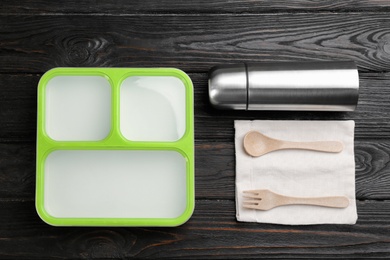 Photo of Thermos, lunch box and cutlery on black wooden table, flat lay