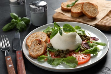 Photo of Delicious burrata salad with tomatoes, arugula and pesto sauce served on dark grey table