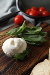 Photo of Delicious burrata cheese with basil on wooden board