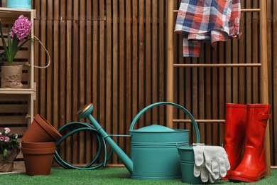 Photo of Composition with different gardening tools on artificial grass at wooden wall. Space for text