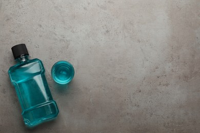 Bottle and glass with mouthwash on grey table, flat lay. Space for text