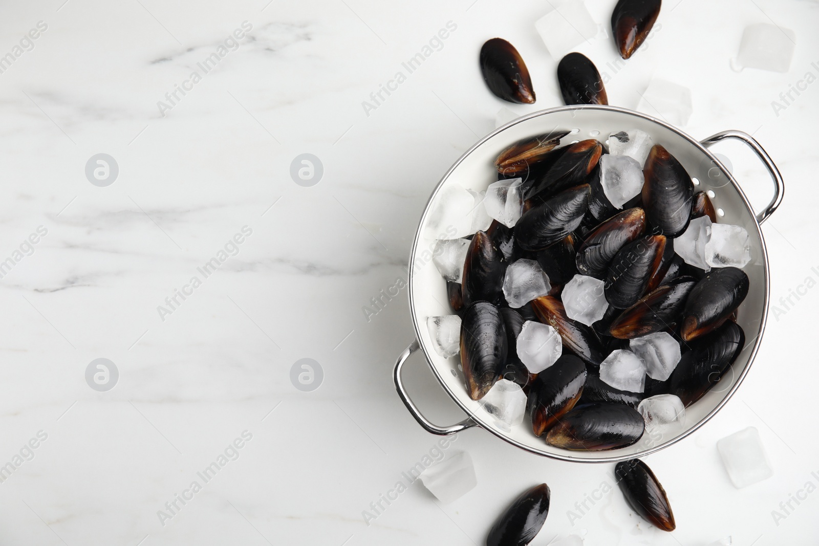 Photo of Colander with raw mussels and ice on white marble table, flat lay. Space for text