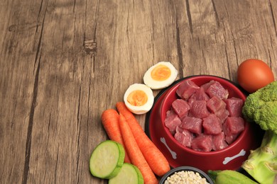 Raw meat in bowl and healthy products for pet on wooden background, above view. Space for text