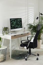 Comfortable workplace with modern computer and green plants in room. Interior design