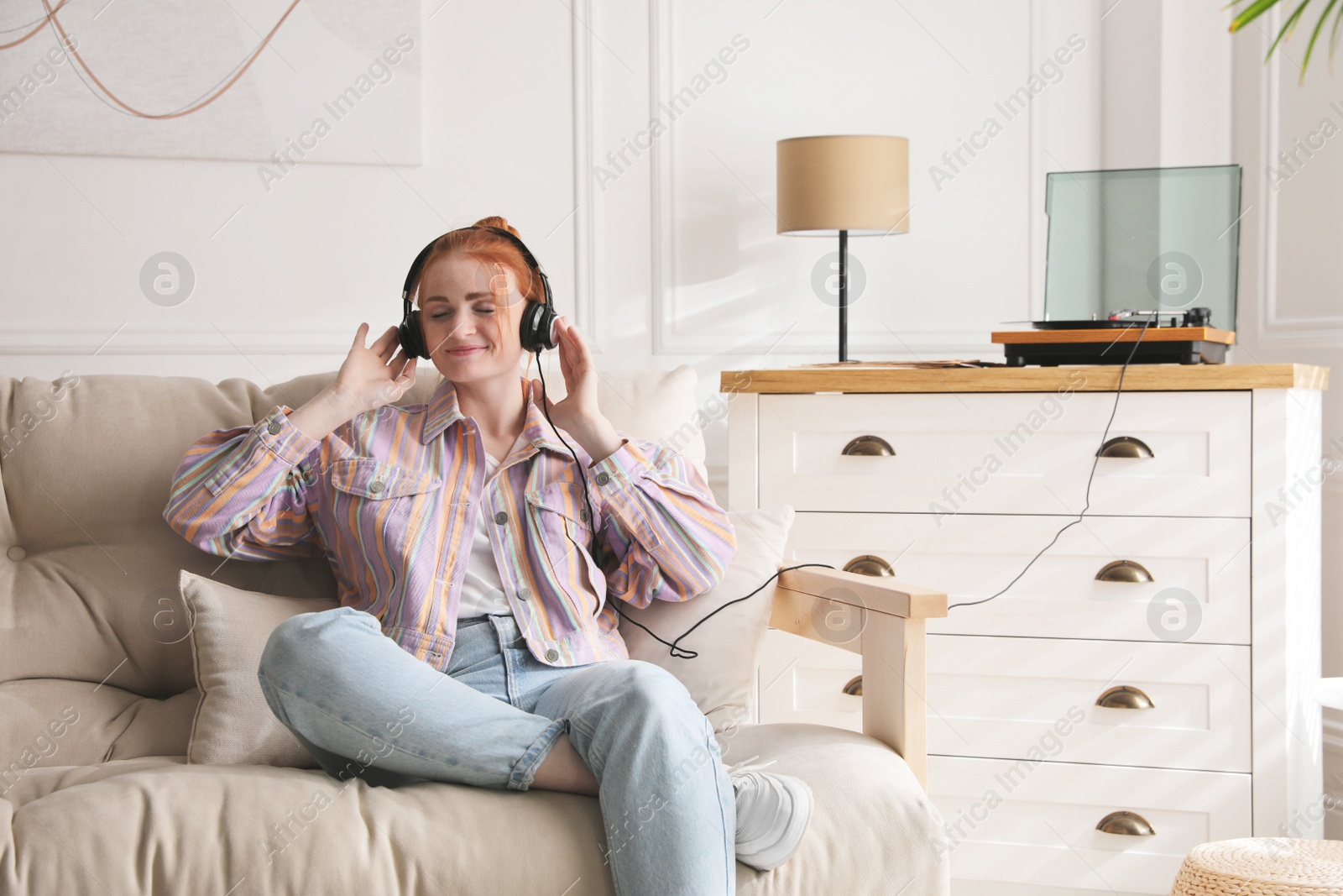 Photo of Young woman listening to music with turntable in living room