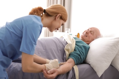 Nurse making injection to elderly man on bed indoors. Medical assistance