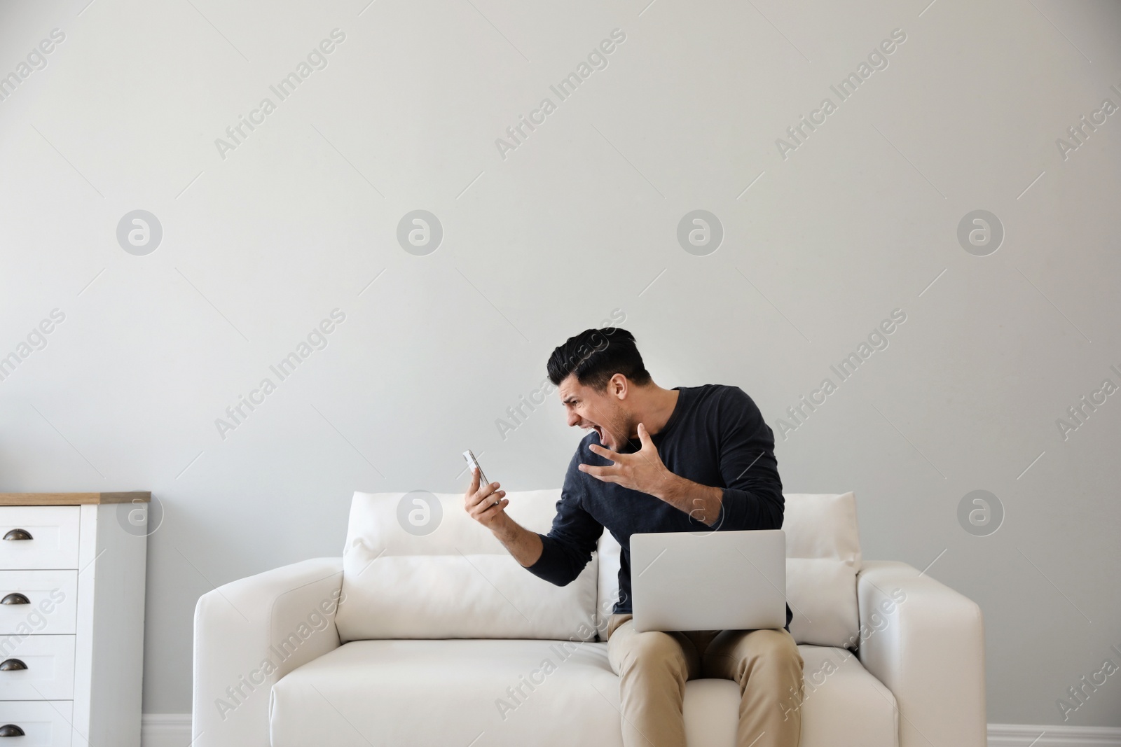 Photo of Emotional man with smartphone and laptop at home