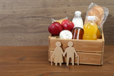 Photo of Humanitarian aid for elderly people. Different donation food products and figures of senior couple on wooden table. Space for text