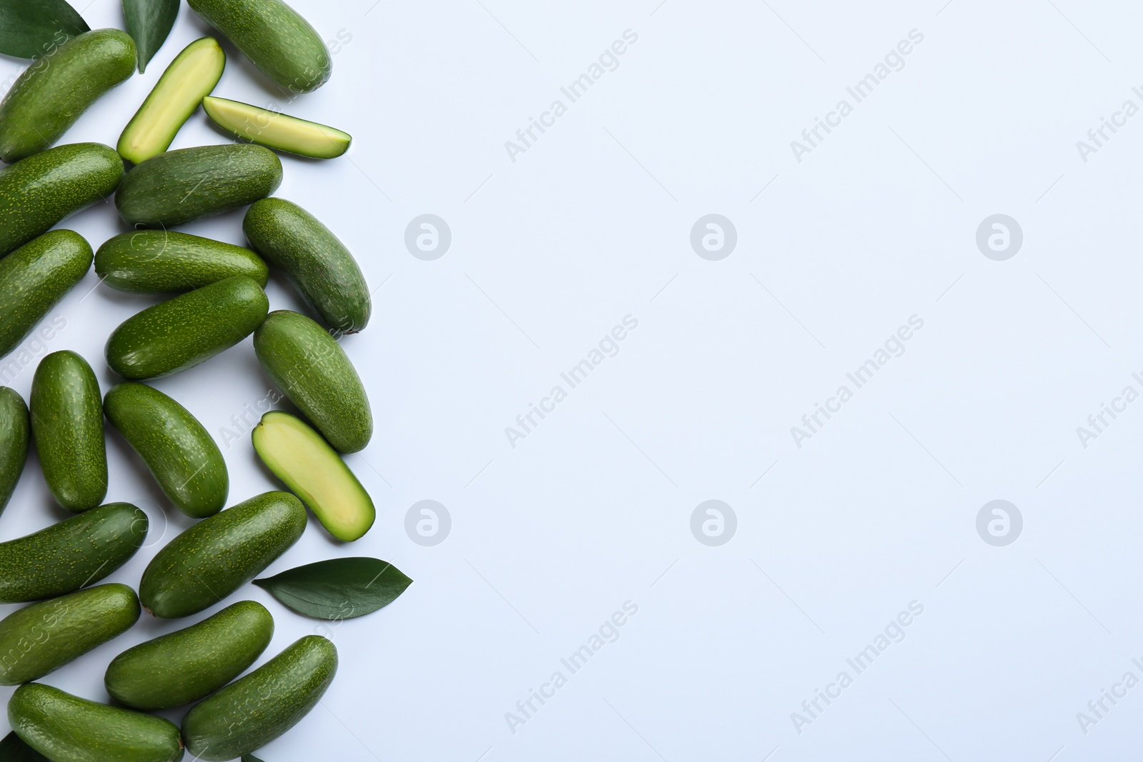 Photo of Whole and cut seedless avocados with green leaves on light background, flat lay. Space for text