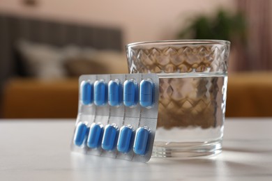 Photo of Glass of water and pills on white table indoors, closeup. Potency problem concept