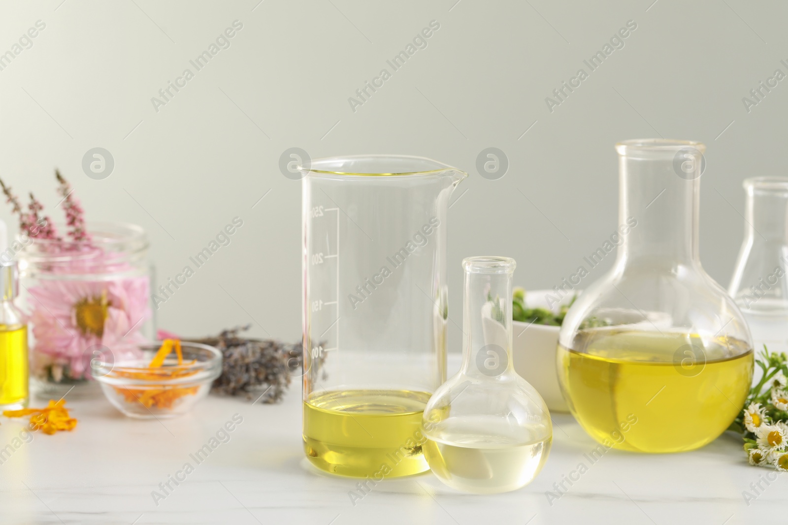 Photo of Cosmetic oil, laboratory dishware and flowers on white table
