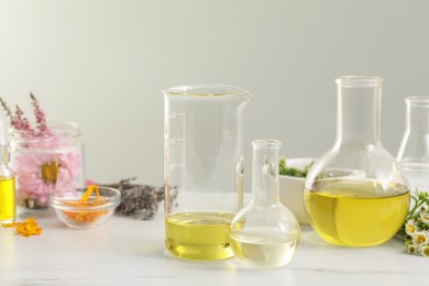 Cosmetic oil, laboratory dishware and flowers on white table