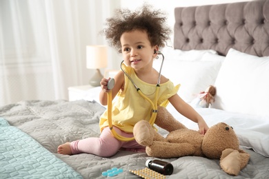 Photo of Cute African American child imagining herself as doctor while playing with stethoscope and toy bunny at home