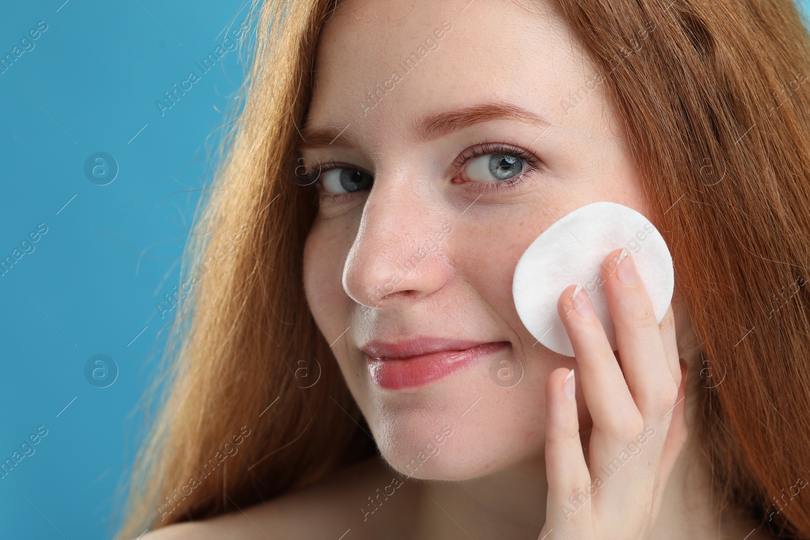 Photo of Beautiful woman with freckles wiping face on light blue background, closeup