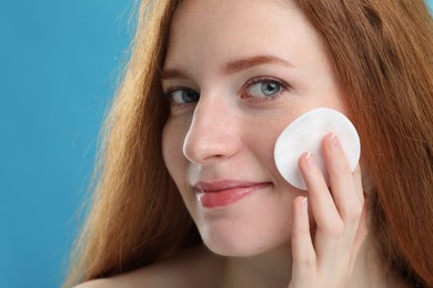 Beautiful woman with freckles wiping face on light blue background, closeup