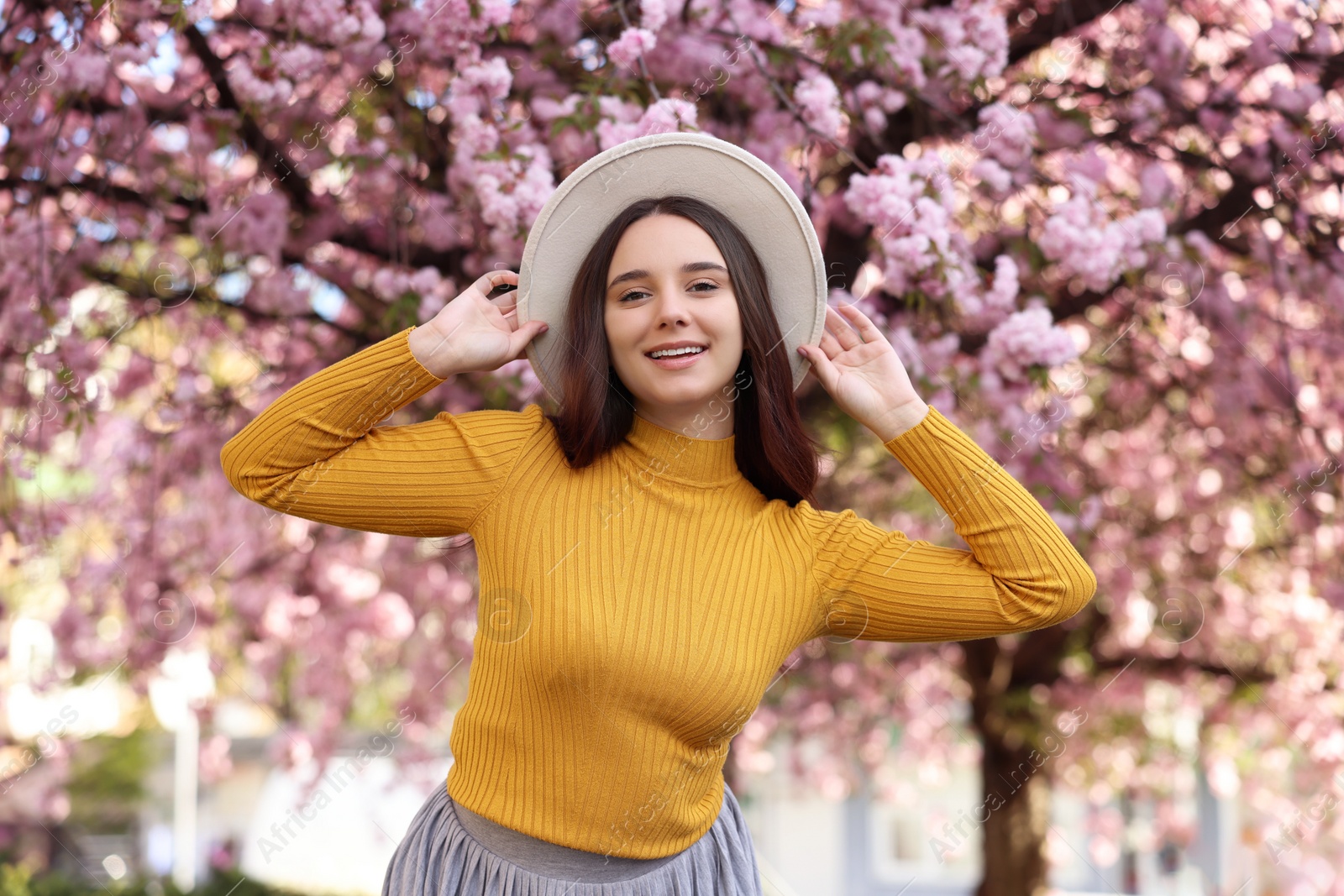 Photo of Beautiful woman in hat near blossoming tree on spring day