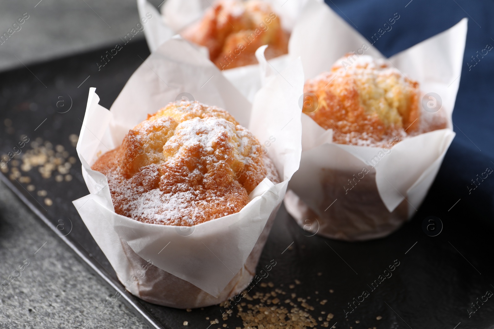 Photo of Delicious muffins with powdered sugar on grey table, closeup