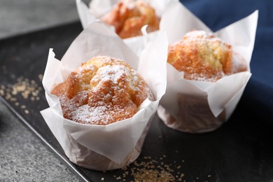 Delicious muffins with powdered sugar on grey table, closeup