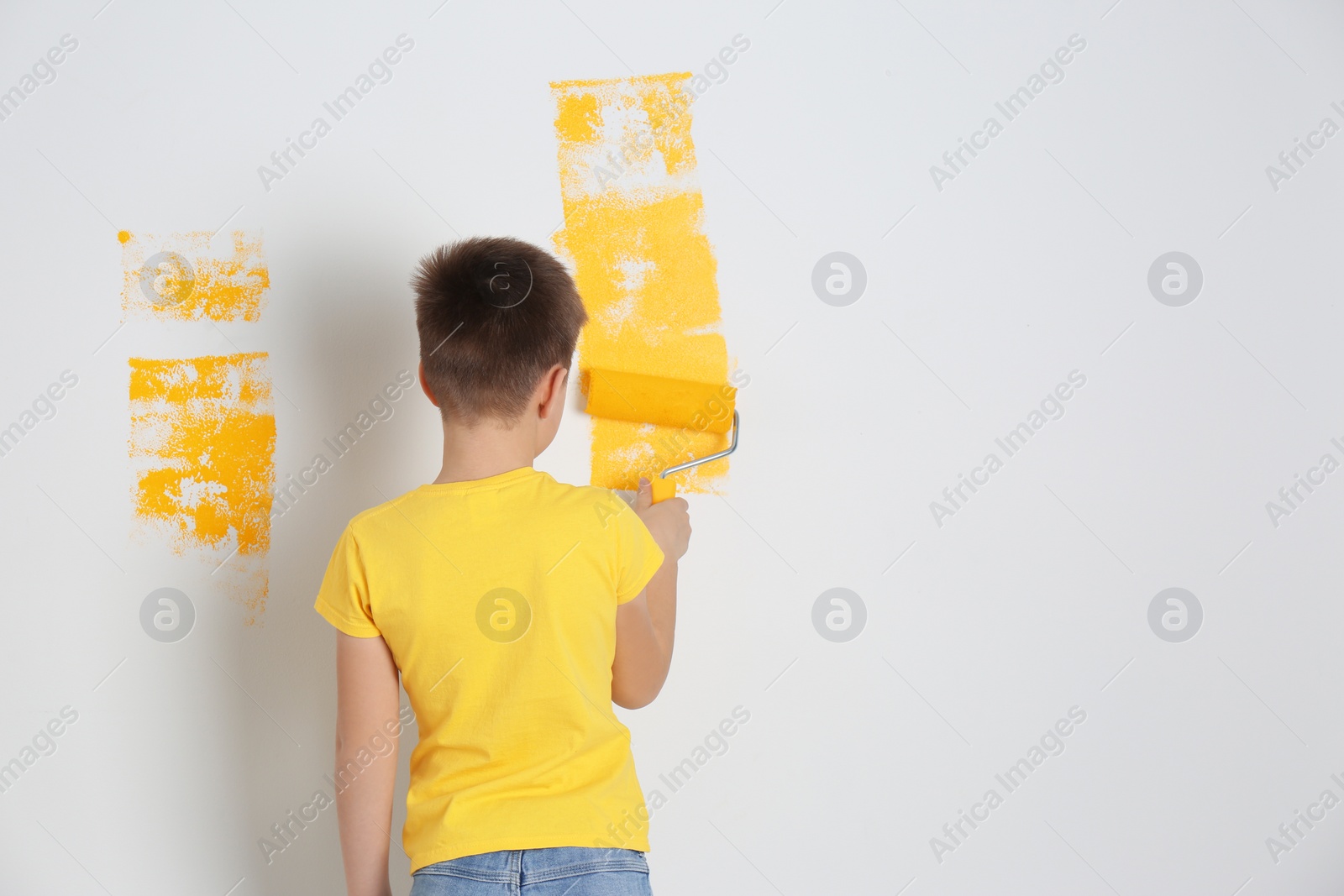 Photo of Little child painting wall with roller brush indoors